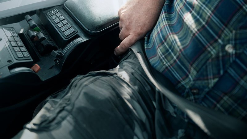 Mann i kjører traktor som tar på seg setebelte.
