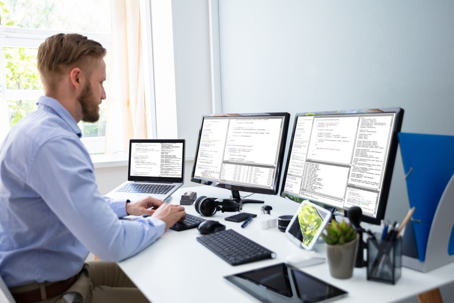 Bildet viser en mann som sitter foran tre skjermer på et kontor