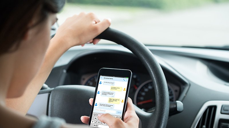 En bilsjåfør som sitter og skriver på en mobiltelefon mens han eller hun kjører. 