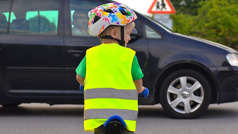 Bildet viser en liten gutt som sykler med hjelm og refleksvest
