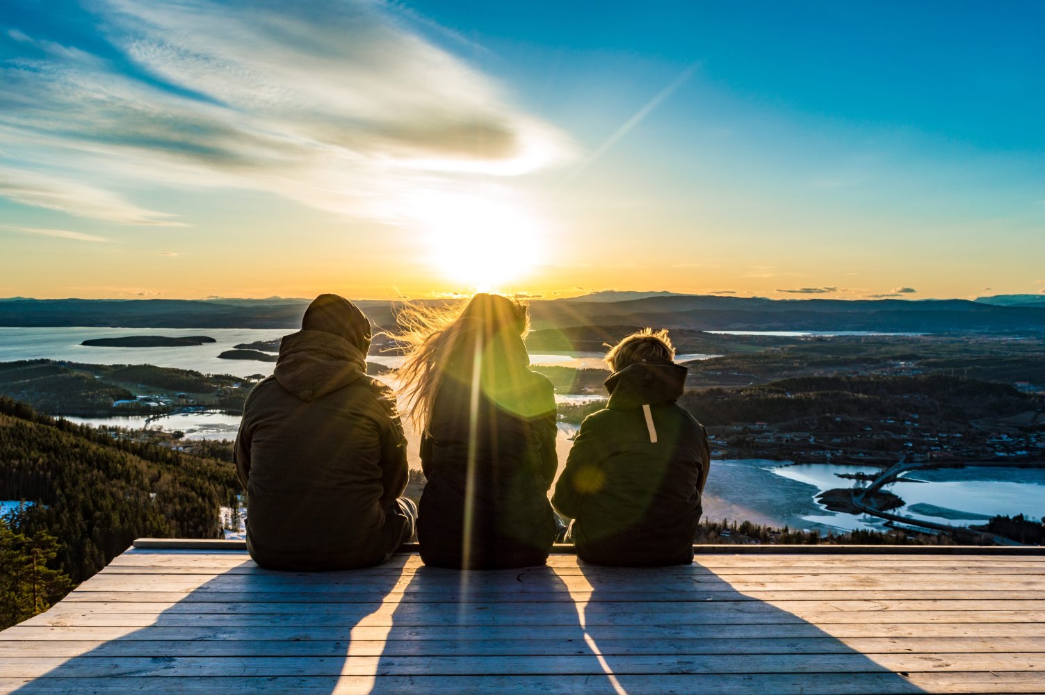 Bildet viser en mor og to barn som sitter på en platting å ser på utsikten.