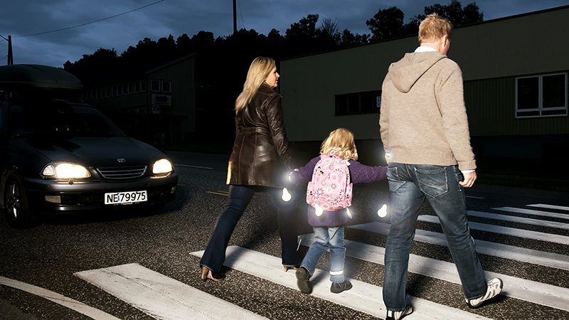 Familie med refleks går over fotgjengerfelt på kvelden