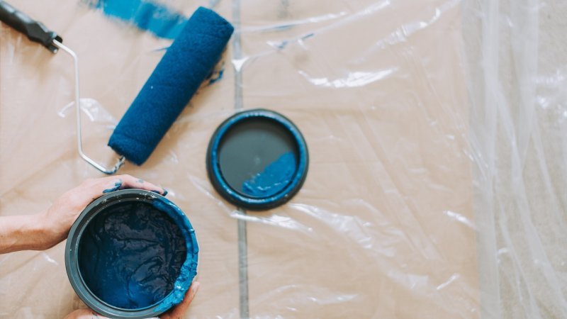 Blå maling og rulle er klar til bruk.  Gulvet er dekket med plast.