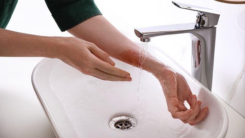 Dame holder hånd under lunkent vann i vasken.