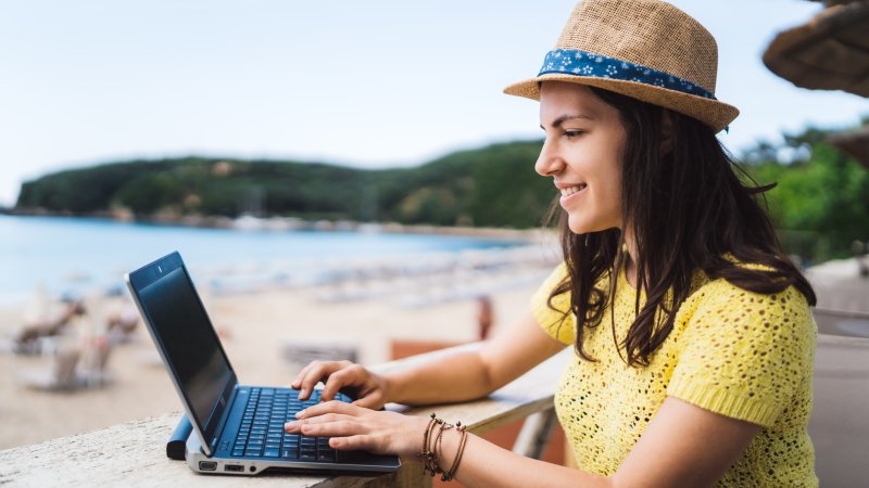 Unge dame sitter med PC på et bord ved en sandstrand.