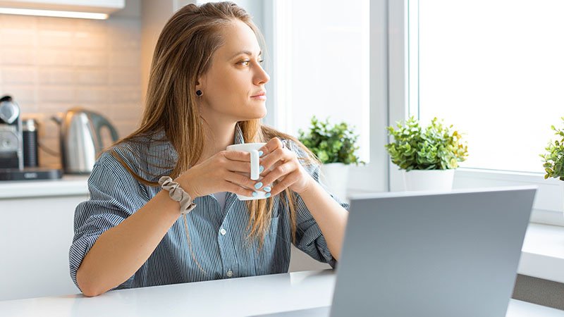 Betenkt dame drikker kaffe og ser ut av vinduet.