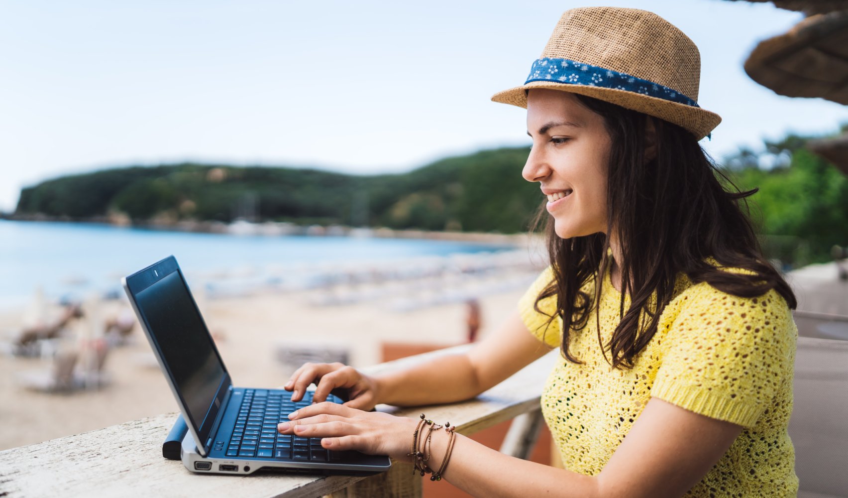 Unge dame sitter med PC på et bord ved en sandstrand.