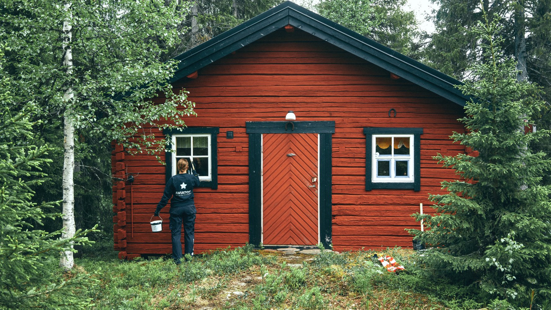 Dame maler rød hyttevegg i skogen