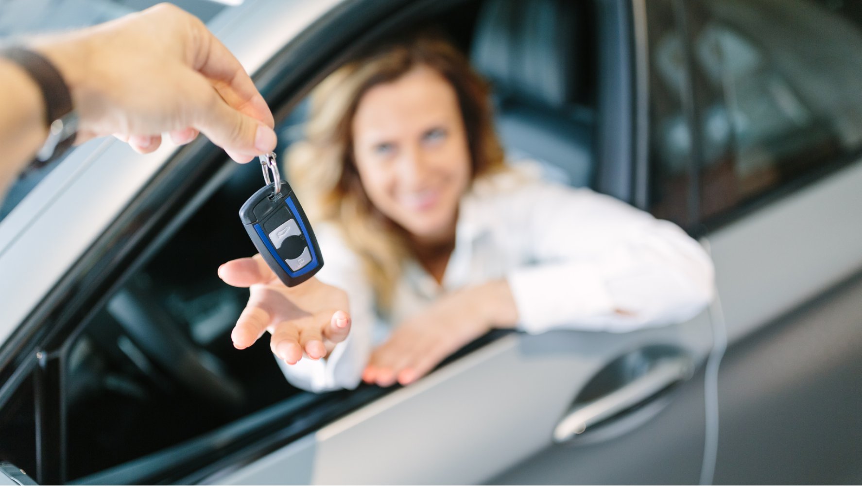 En kvinne, som sitter i en bil, strekker seg mot en hånd med bilnøkler.