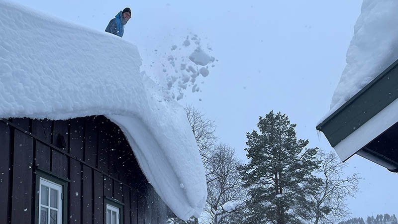 Ungdom som måker snø ned fra hustak.