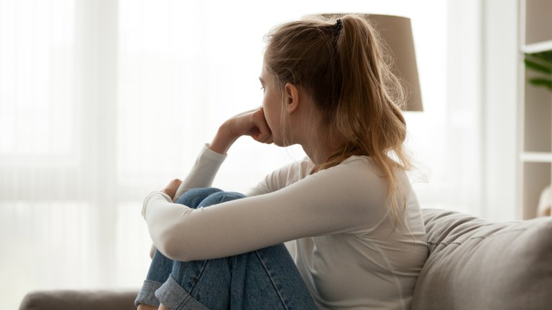 Bildet viser en ung jente som sitter i sofaen og ser bort. 