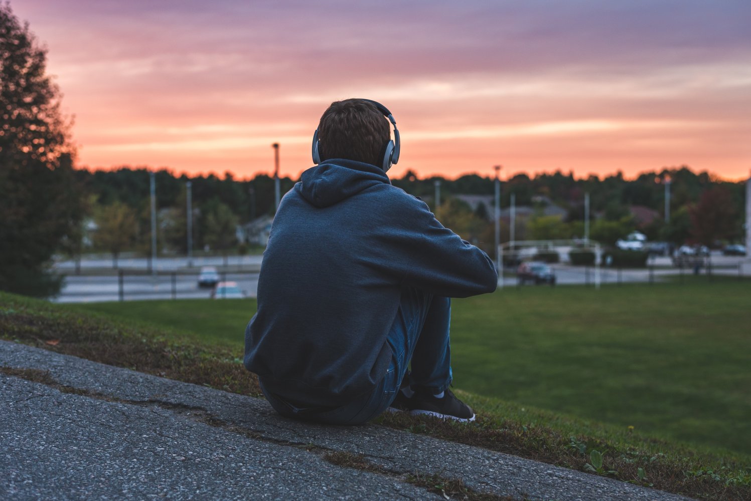 En ungdom sitter alene og ser utover en tom fotballbane.