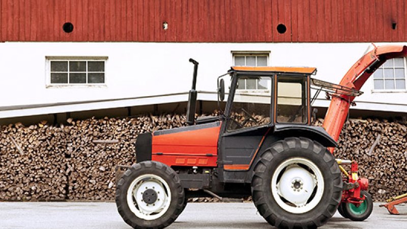 Rød traktor foran låve og vedstabel.