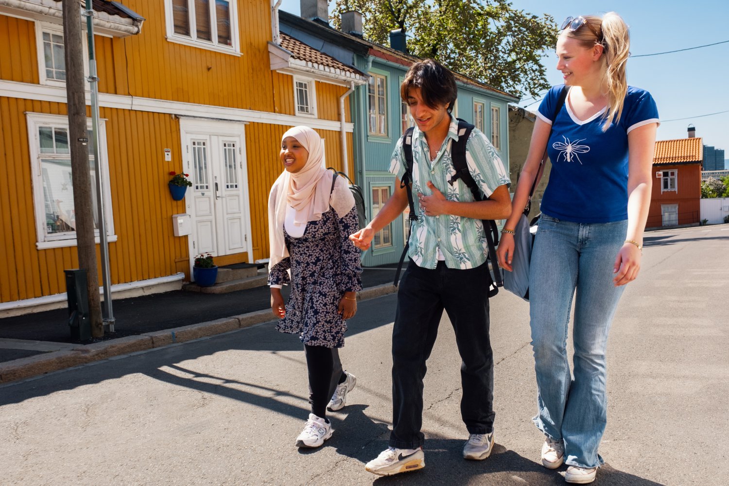 Tre unge mennesker, to kvinner og en mann, snakker og ler mens de går nedover gata.