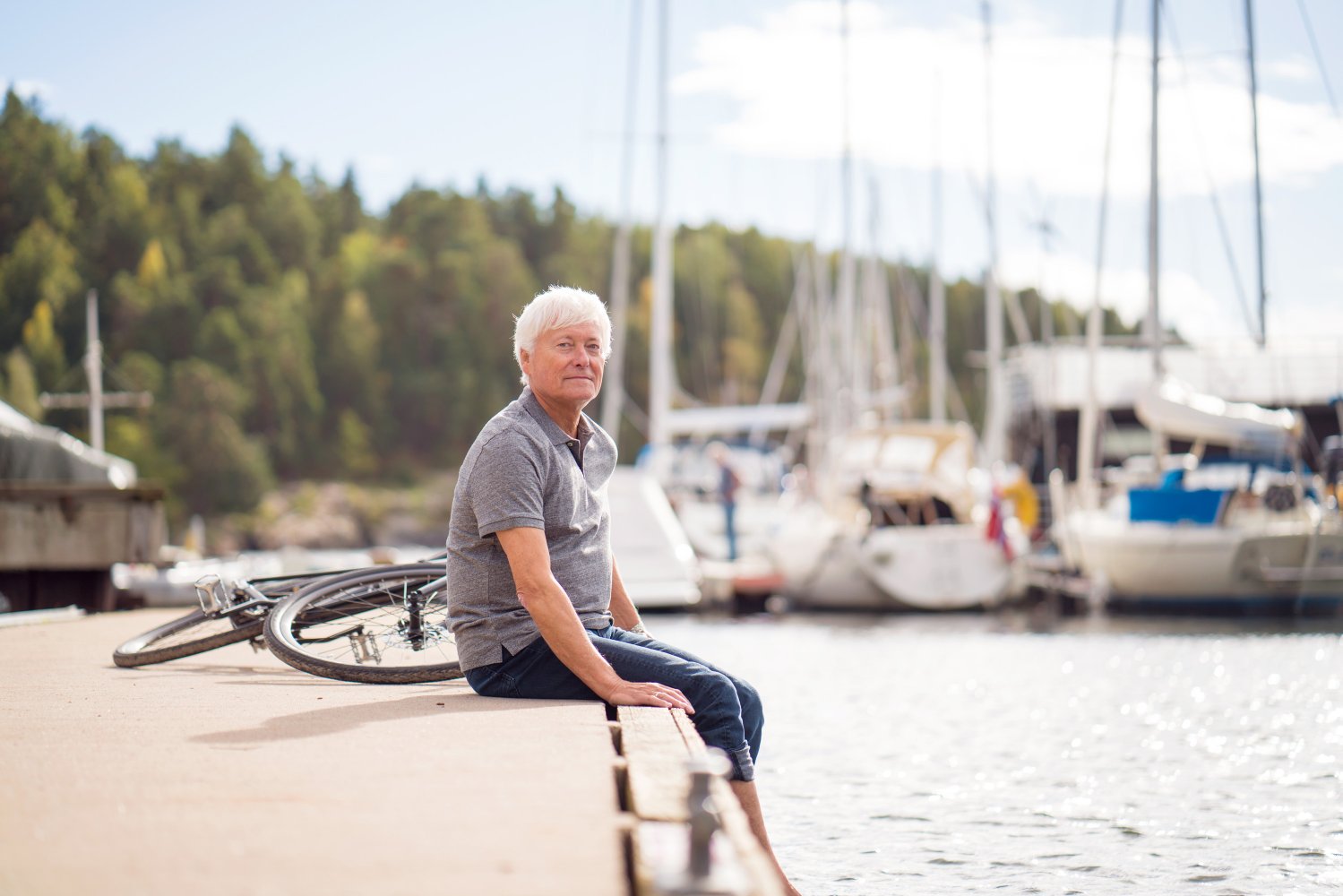 Senior sitter på brygge. Vann, båter og sol