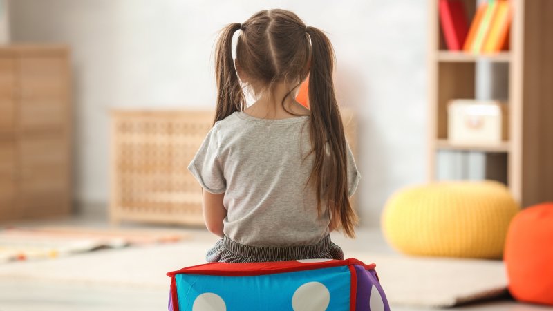 En liten jente som sitter med ryggen til i et lekerom