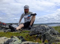 Rolf erik på sykkeltur. Sitter på stein. Utsikt over vann og natur
