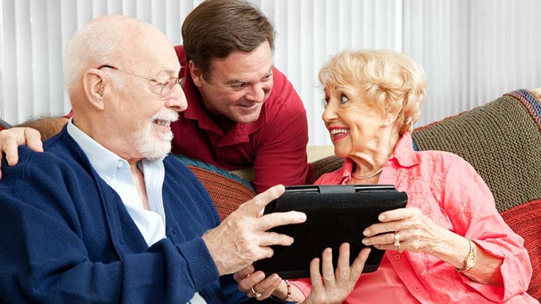 To eldre personer får hjelp av yngre mann på iPad.