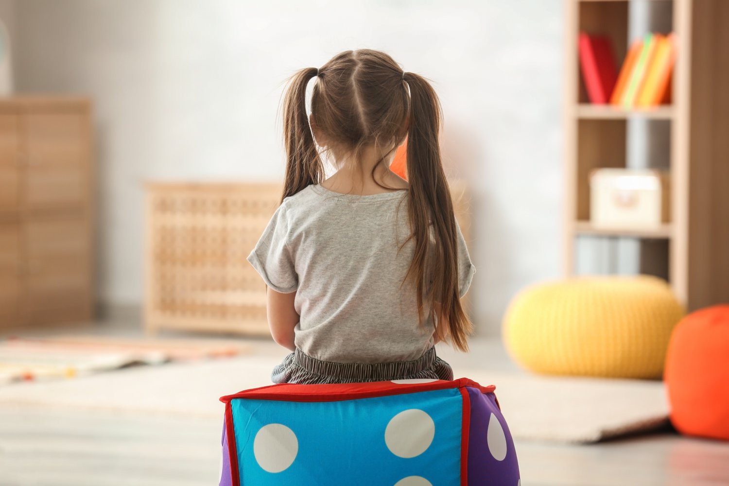 En liten jente som sitter med ryggen til i et lekerom