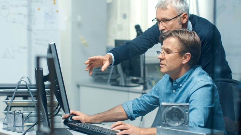 Bildet viser to eldre menn som ser på en datamaskin