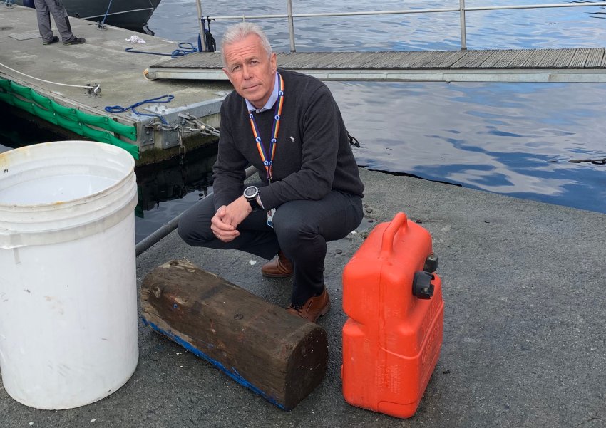 Arne Voll sitter på huk på bryggekanten med en tømmerstokk og en plastikkdunk som er funnet flytende i sjøen.