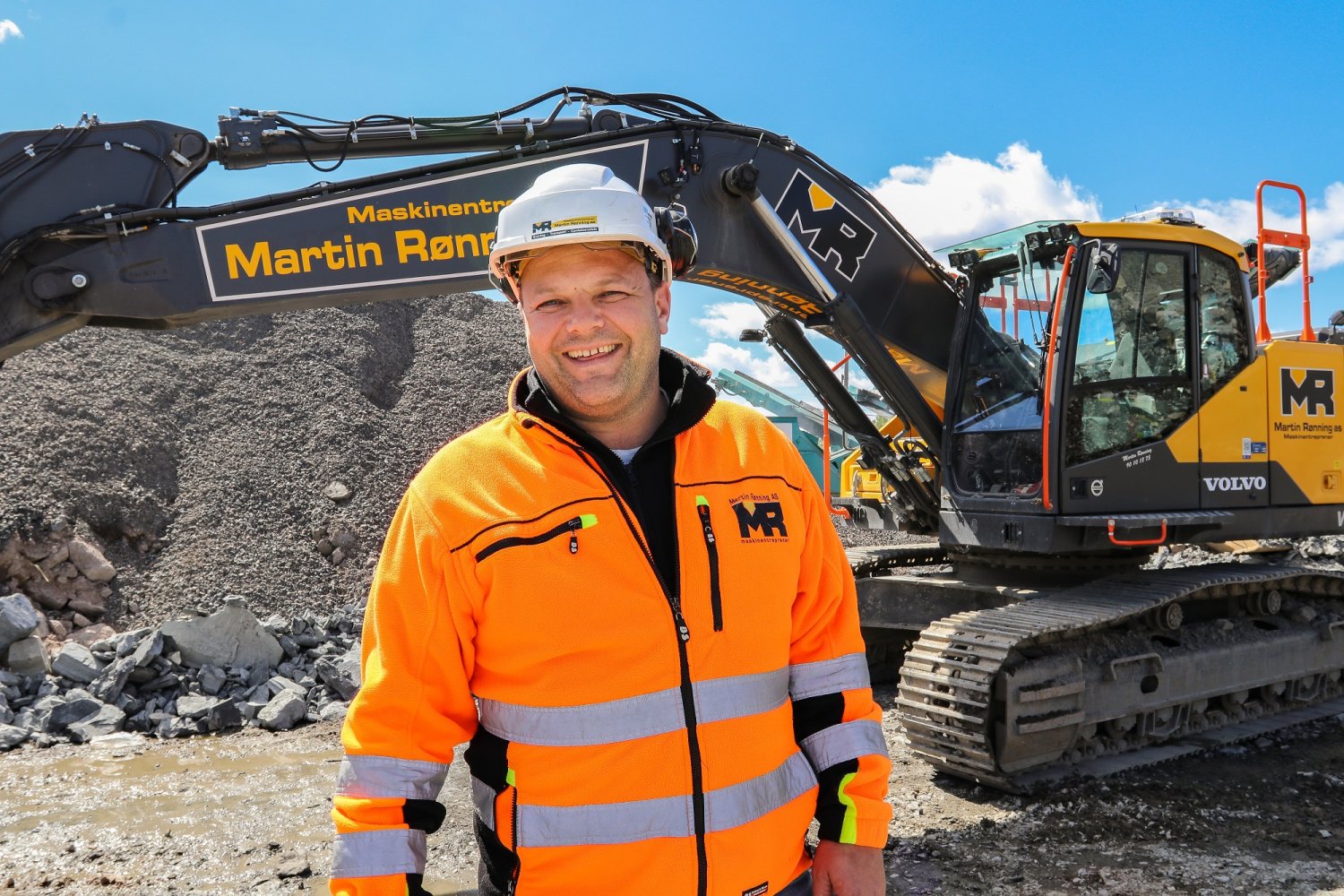 Svein-Erik Ryen står foran en gravemaskin og smiler.