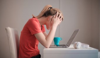 Fortvilet jente som sitter ved bord og ser ned i PCen med hendene på hodet