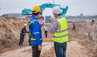 Et byggeområde hvor noen jobber med maskiner og noen sjekker en laptop