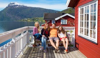 Fornøyd familie på hytteterrasse med fjord og fjell i bakgrunnen.
