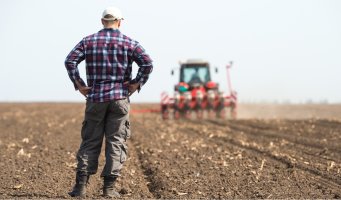 Bonde som ser utover åker. Traktor i bakgrunnen.