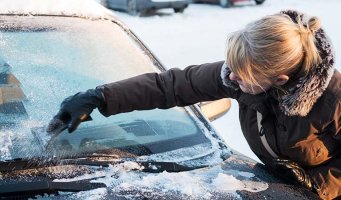 Dame skraper nediset frontrute på bil