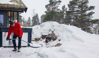 Mann som måker snø utenfor en hytte