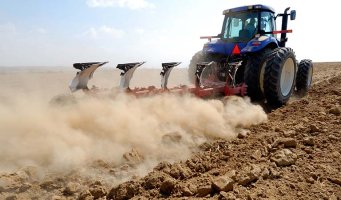 Traktor ploger på tørt jorde så støvet spruter