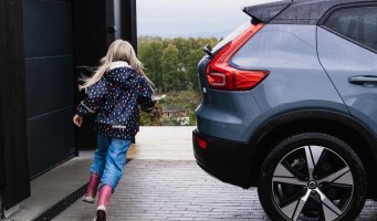 Barn løper rundt bil parkert utenfor garasje.