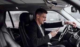 Ung mann sjekker mobilen bak rattet i en bil.