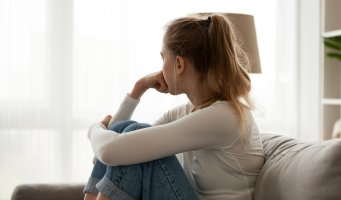 Bildet viser en ung jente som sitter i sofaen og ser bort. 