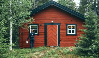 Dame maler rød hyttevegg i skogen
