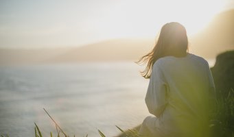 Jente sitter i gresset og ser utover havet