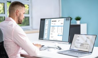 Mann på kontor med flere skjermer med fakturaer.