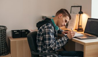 Bildet viser en ung gutt som sitter hjemme og jobber med skole
