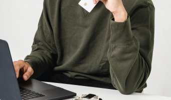 Bankkort i hånden foran PC-skjerm.