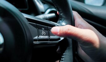 Mann som holder en hånd på bilrattet og en finger på cruisekontroll-knappen.